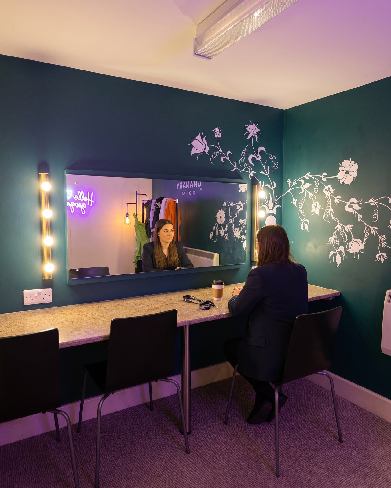A presenter at the dressing-room mirror between the globe bulbs