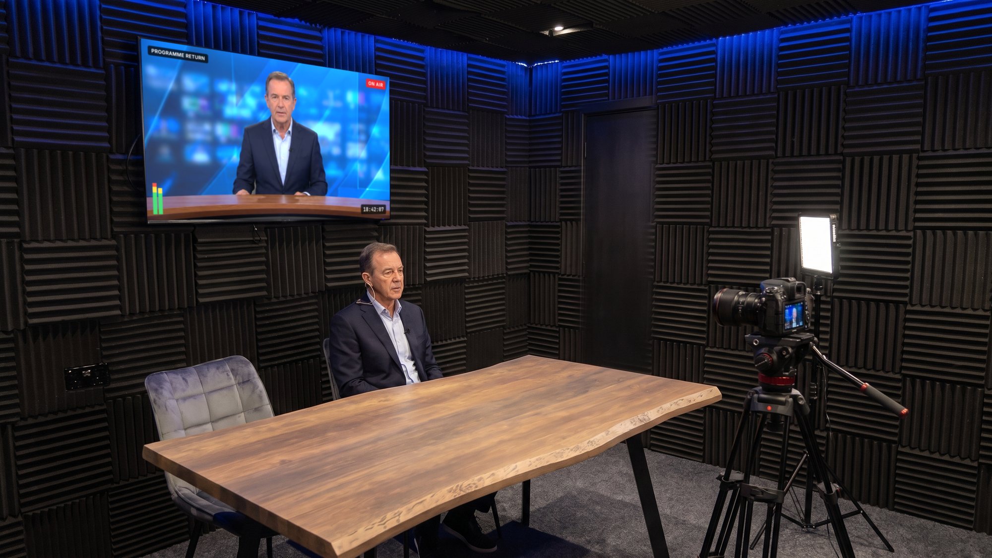 A spokesperson doing a down-the-line interview, the programme feed on the wall screen