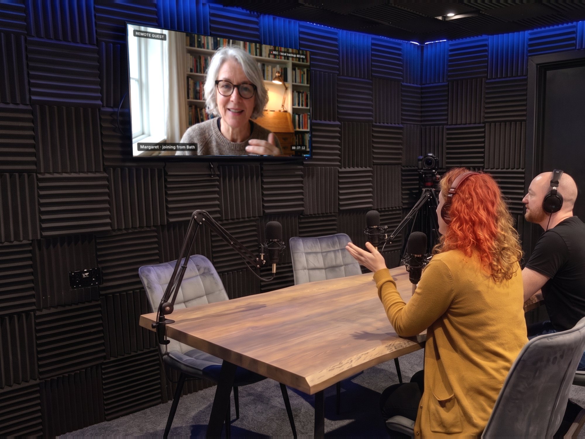 A hybrid podcast: two hosts in the room and a remote guest on the wall screen