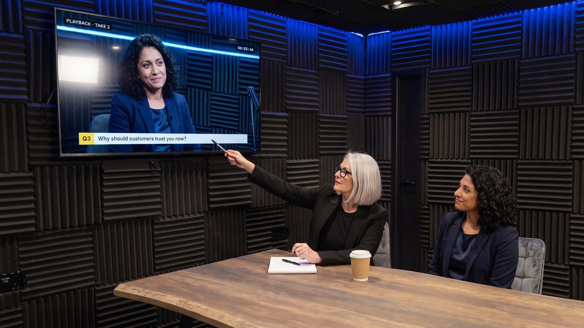 A media trainer reviewing interview playback with a client on the wall screen