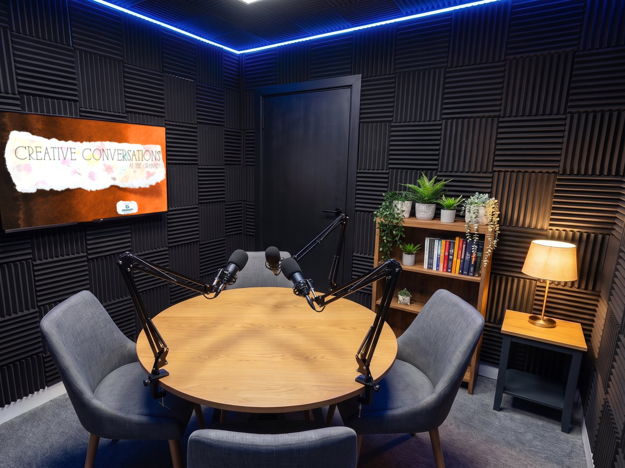 A round table with four microphones on boom arms, Creative Conversations artwork on the screen