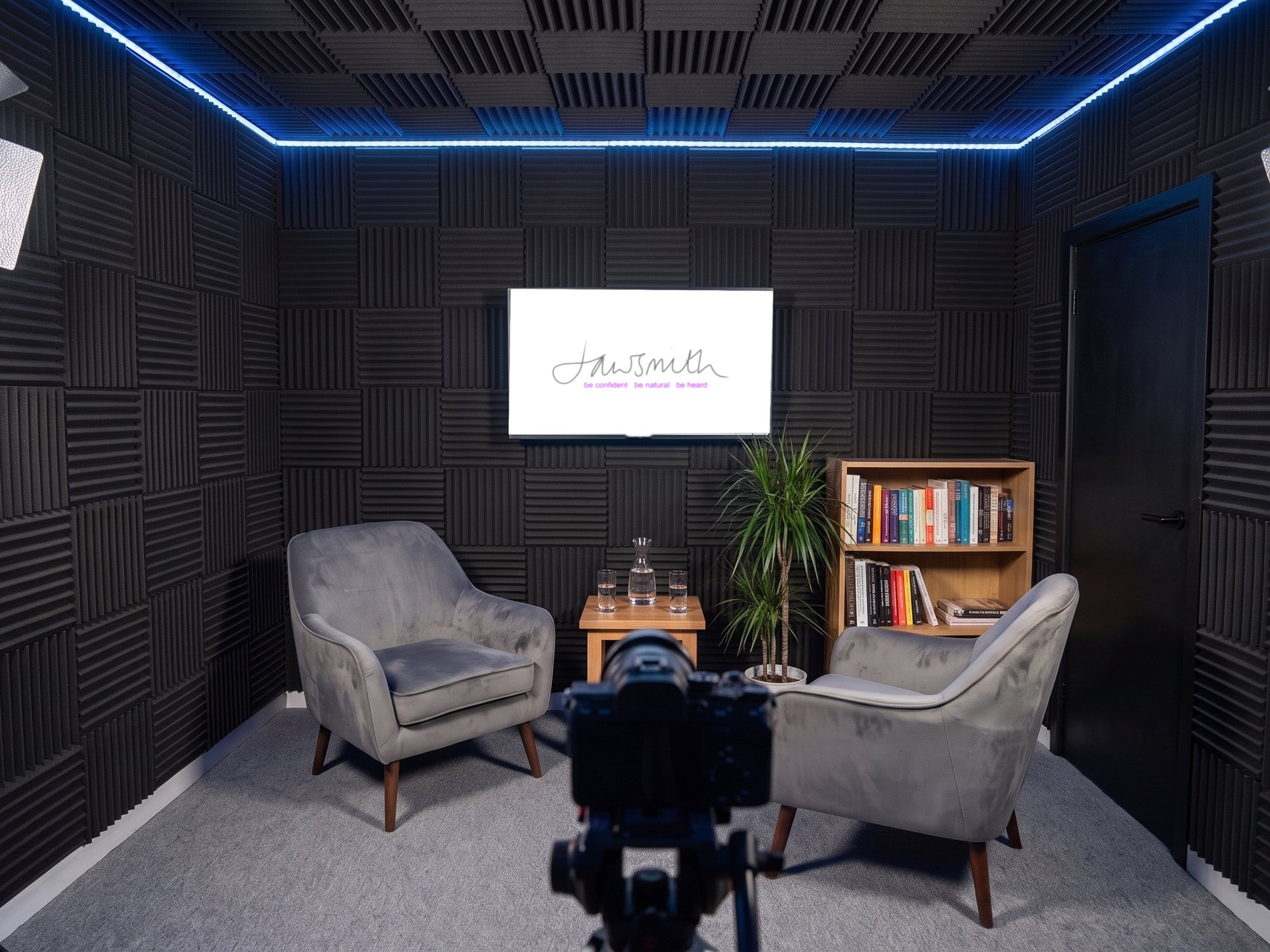 An interview corner with two armchairs and a camera on a tripod, Jawsmith artwork on the screen