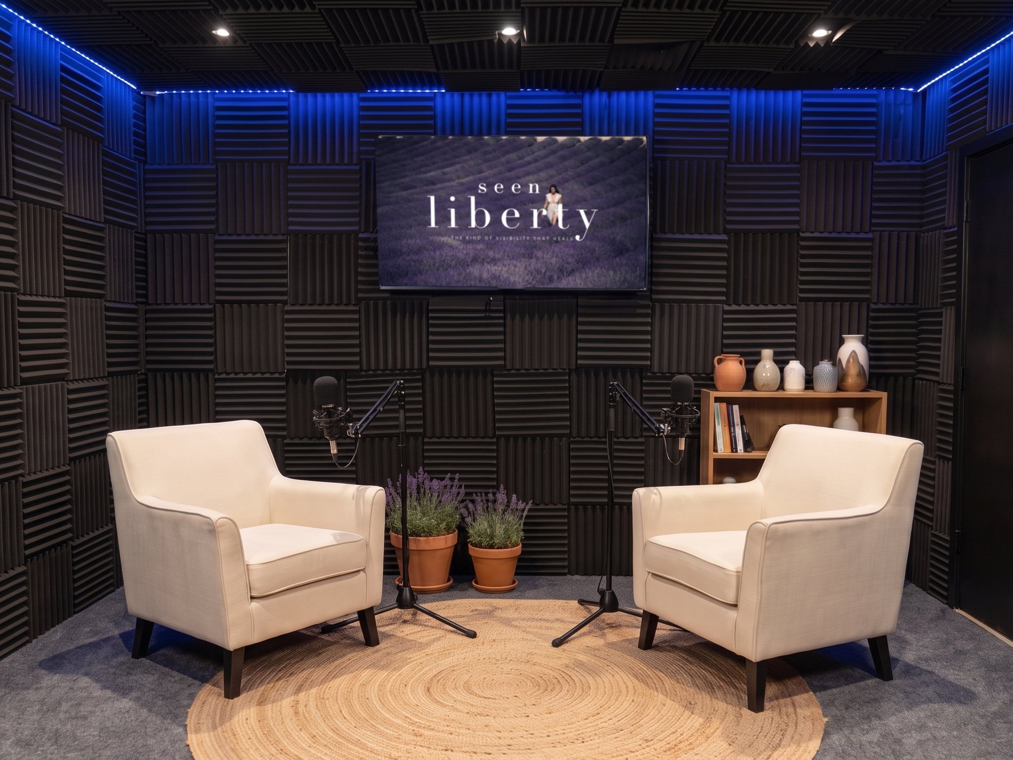 Two cream armchairs on a jute rug with floor-stand microphones, Seen Liberty artwork on the screen