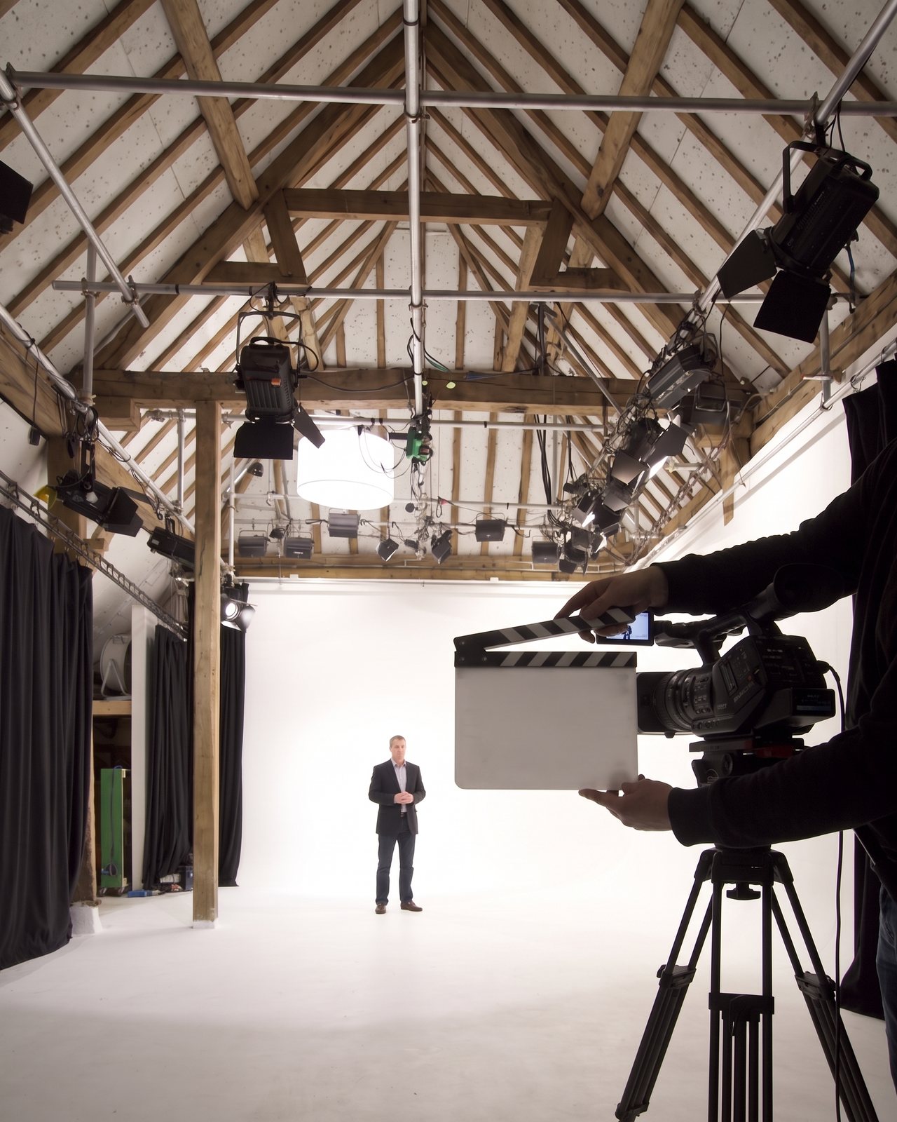 A clapperboard held up in front of a camcorder, a presenter on the cove behind