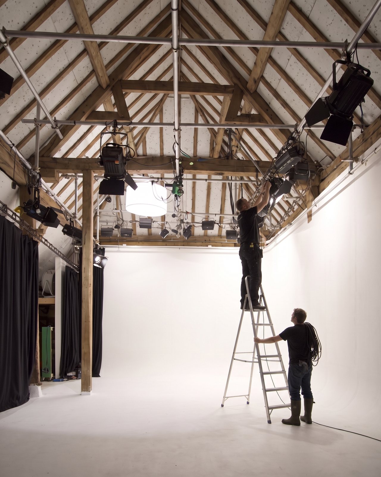 A gaffer on a stepladder clamping a fresnel to the grid under the oak roof