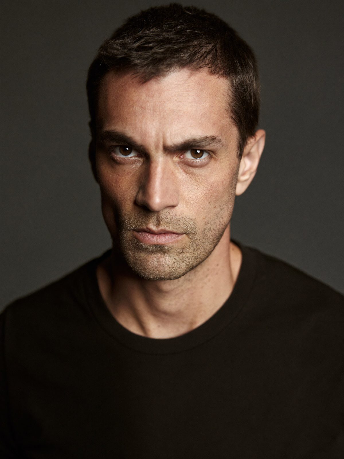 Example actor headshot, a serious man with stubble on dark grey