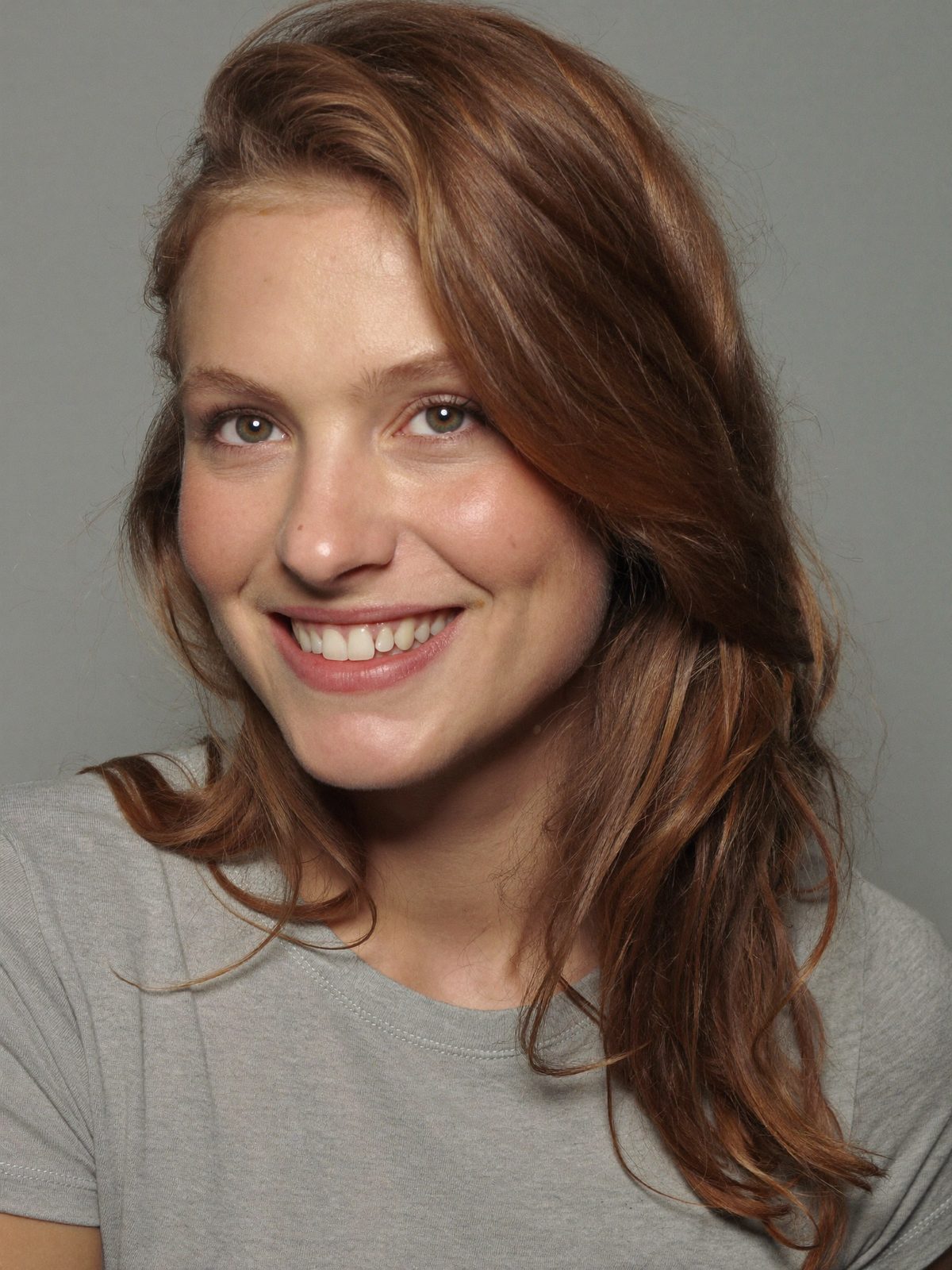 Example actor headshot, a smiling young woman with auburn hair on grey