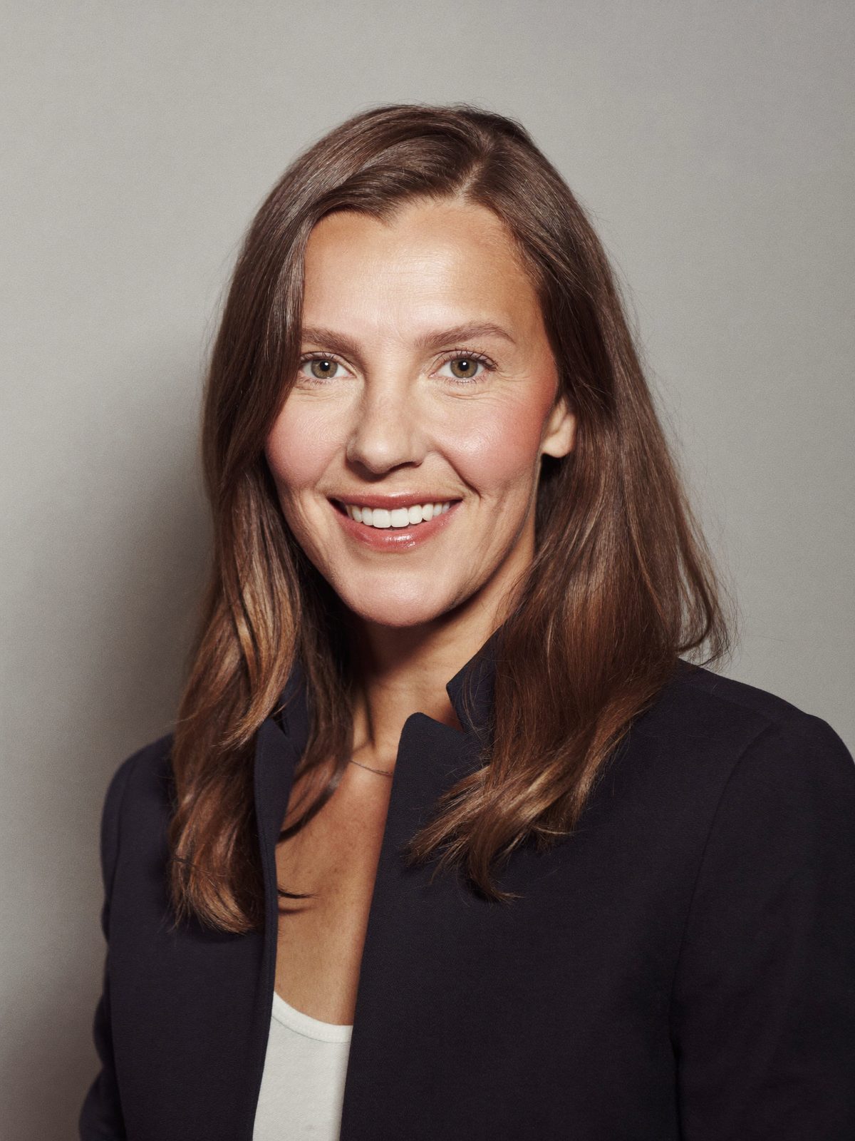 Example headshot, a woman in a navy blazer on a light grey background