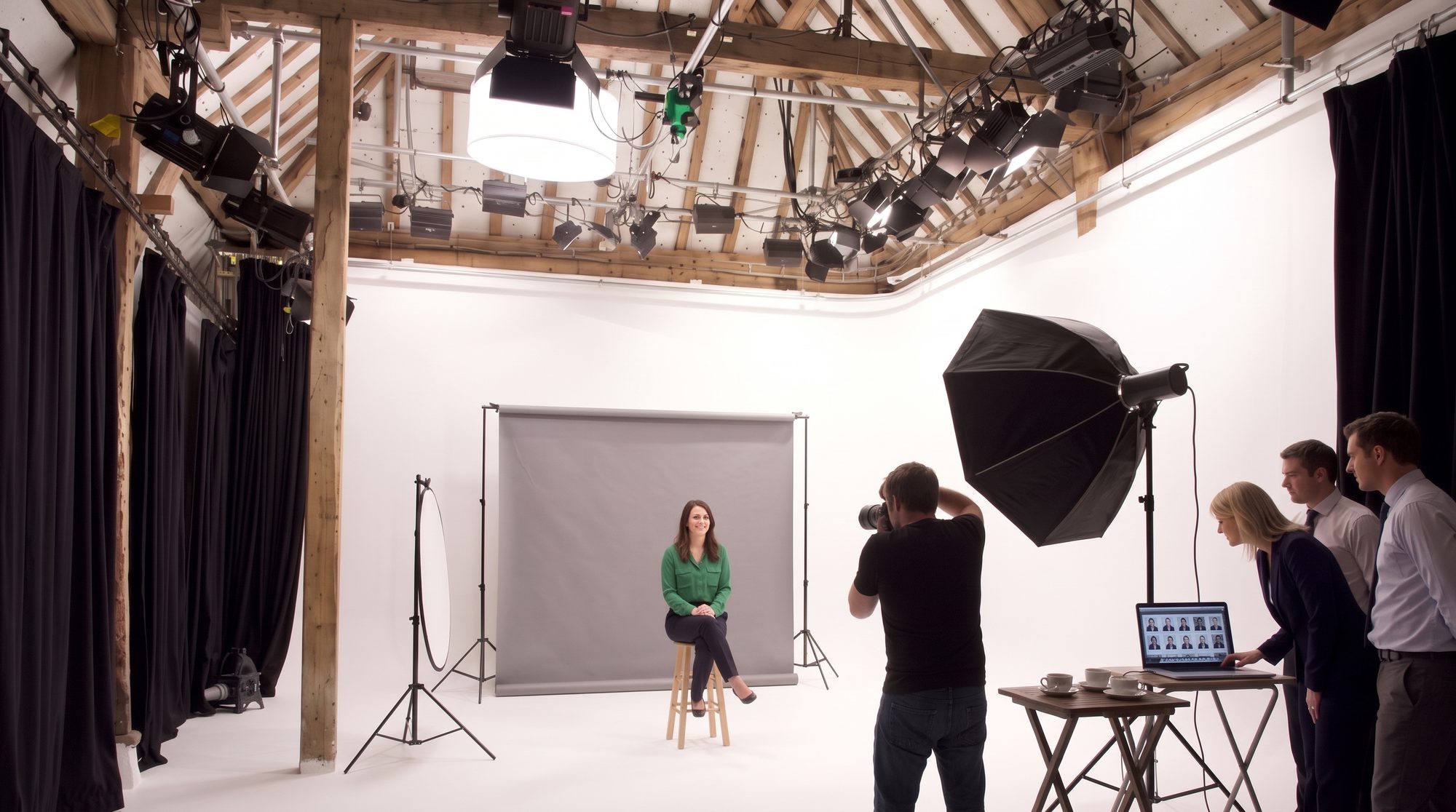 A company headshot day, one colleague on the stool while three others check the pictures on a laptop