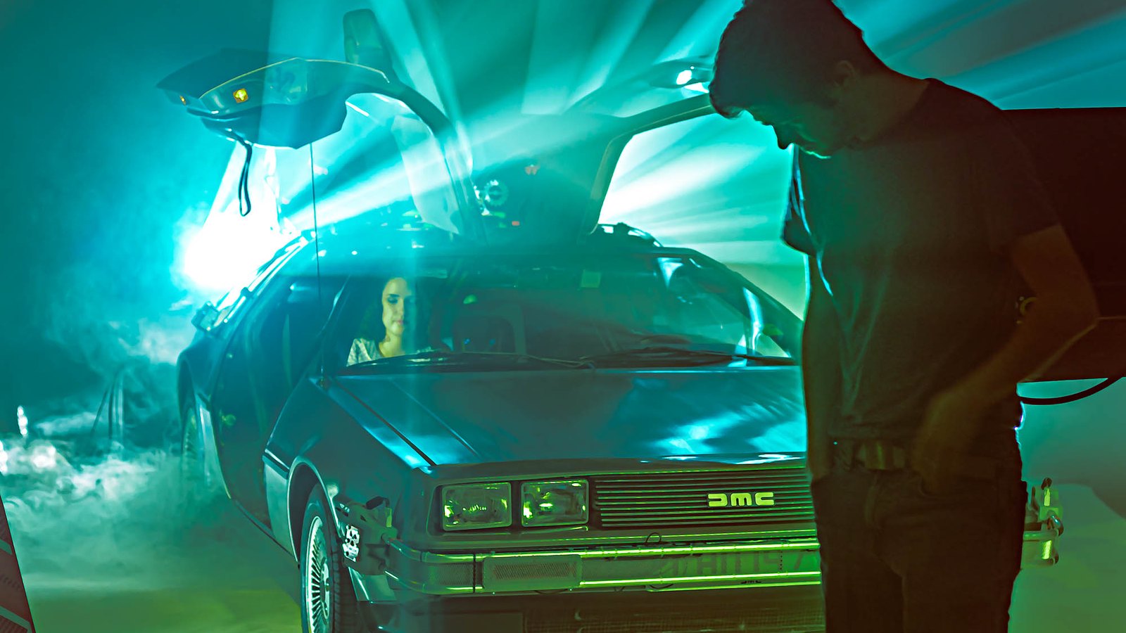 Crew adjusting a light beside the DeLorean on the hazed stage