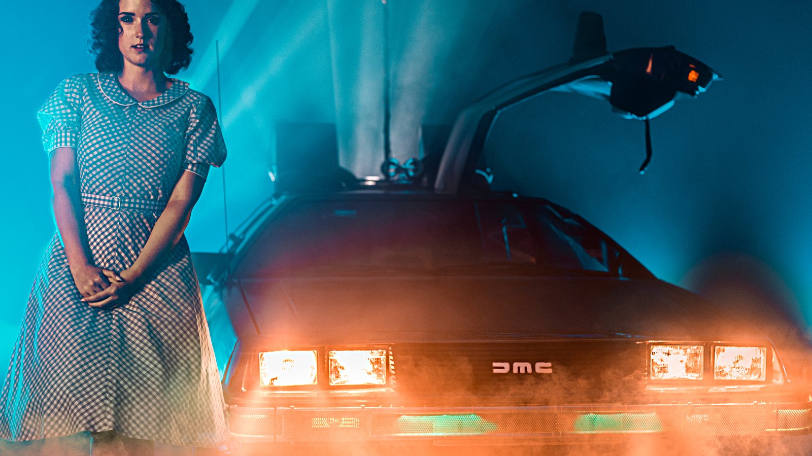 A DeLorean with gullwing doors open in orange and teal light on the studio stage
