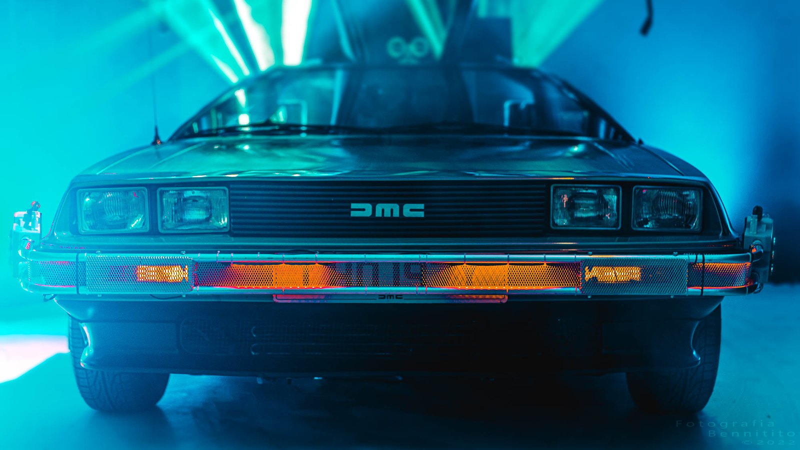 A DeLorean front-on under blue studio light on the blacked-out stage
