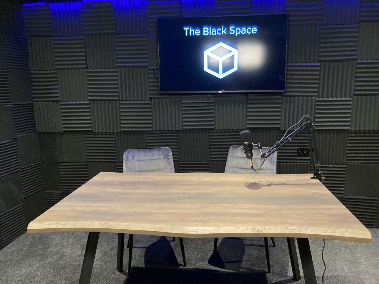 Podcast studio with acoustic foam walls, live-edge table and microphones